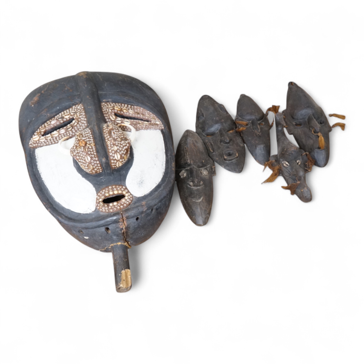 A Papua New Guinea Sepik River large carved wooden mask, painted in black and white and applied with pig tusks and teeth, together with five small plain masks, largest 82cm high